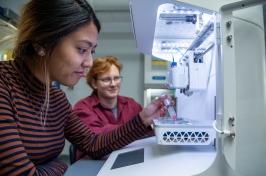 A male 和 female student work together in front of a piece of scientific equipment